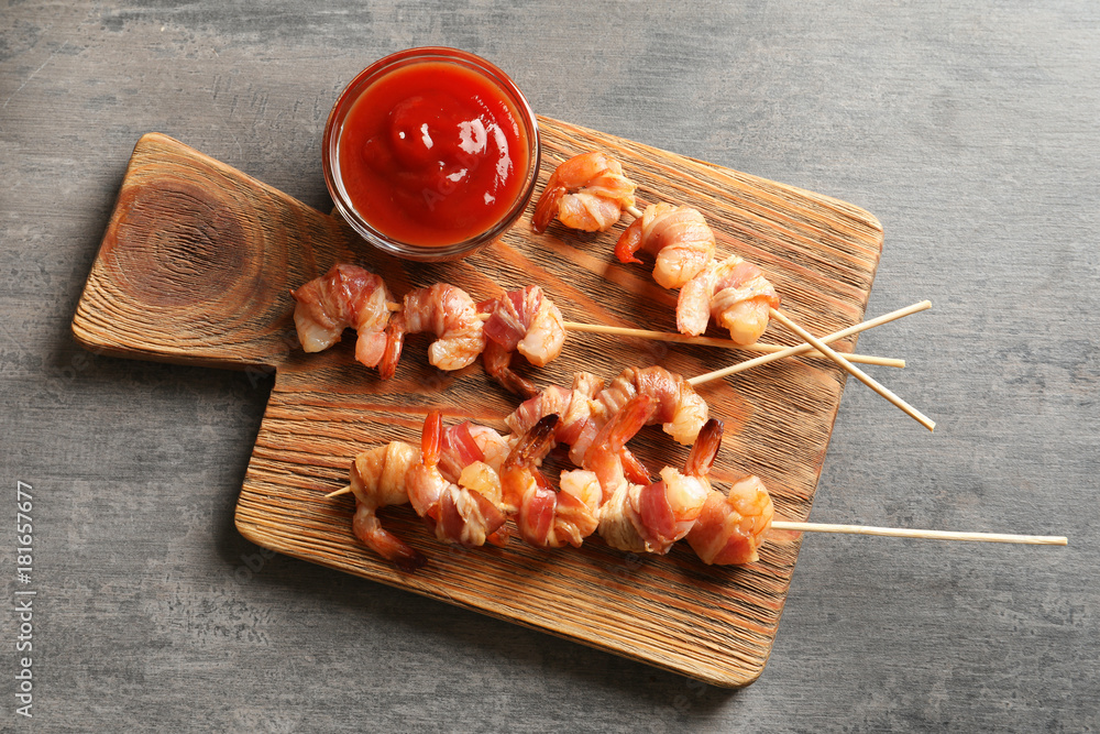 Board with skewered shrimps wrapped in bacon on table