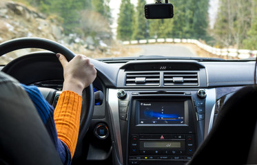 Driver's hand on the steering wheel inside a car on a mountain road