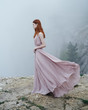 © SHOTPRIME STUDIO - Young beautiful woman in a long pink dress is standing on a cliff of high rock in the fog