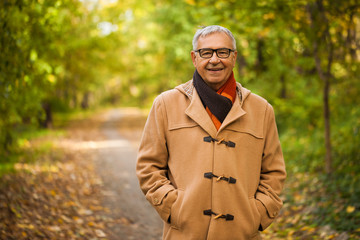 Outdoor portrait of happy senior man wearing coat in autumn. 