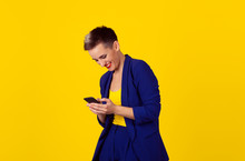 Happy Chat. Closeup Portrait, Happy, Brunette Girl, Smiling, Looking At Company Cell Phone, Isolated Yellow Background. Facial Expression, Reaction. Business Woman Sending Text Message From Her Mobile