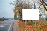 Fototapeta Na ścianę - Empty billboard for advertising poster near road autumn. Trees on background, leaves on the ground. Mock-up.