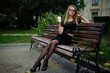 © AS Photo Family - Elegant blonde girl wear on black posing at streets of town, sitting on bench with cup of coffee at hands.