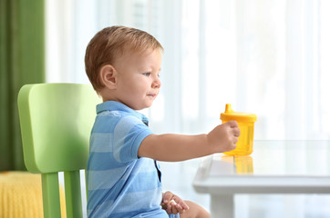 Poster - Adorable baby sitting at table with drinking bottle indoors