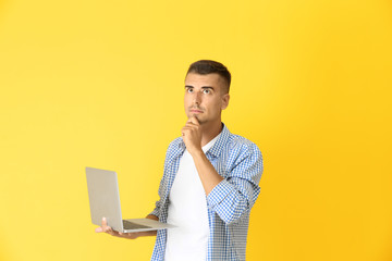 Canvas Print - Thoughtful young man with laptop on color background