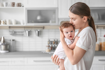 Canvas Print - Young mother holding baby in kitchen