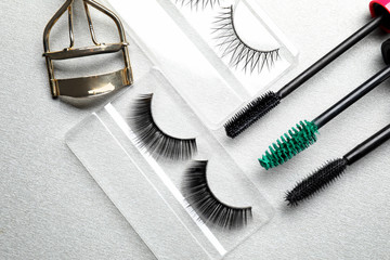 Composition with curler and false eyelashes on light background