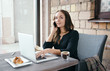 © Krystsina - Young attractive woman sitting in a cafe in the morning before her work and planning tasks for the whole day. Beautiful lady talking on the phone and discussing business strategies with her colleague.