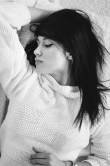 Wall Mural - Brunette calm young woman lying on bed or carpet in white knitted sweater. Monochrome