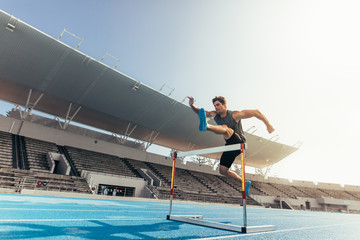 Wall Mural - athlete jumping over an hurdle on running track