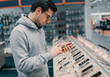 © Igor Kardasov - Happy male customer choosing smartphone in the mobile phone shop. difficult decision. Various choice. He is smiling
