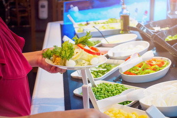 Asian woman choosing vegetable ingredients at salad bar restaurant