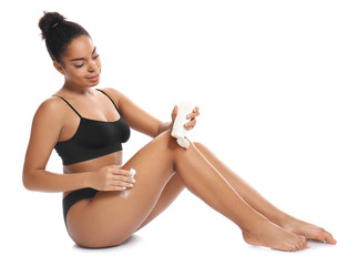 Poster - Beautiful young African American woman applying cream onto skin on white background