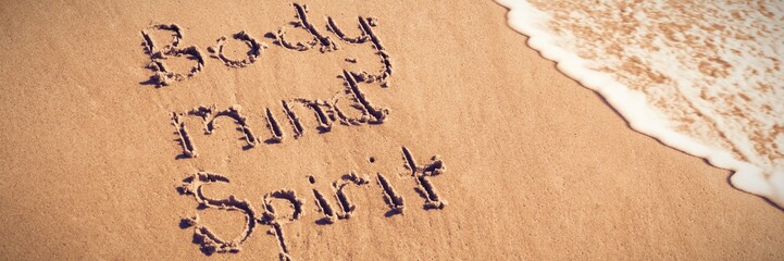 body mind spirit text written on sand with surf
