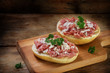 german mettwurst brotzeit, minced pork sausage with onions and parsley garnish on buns, cutting board on a dark rustic wooden background, copy space