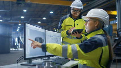 Inside the Heavy Industry Factory Female Industrial Engineer Works on Personal Computer She Designs 3D Turbine Model, Her Male Colleague Talks with Her and Uses Tablet Computer.