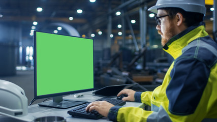 Inside the Heavy Industry Factory Industrial Engineer Works on the Personal Computer with Green Mock-up Screen.