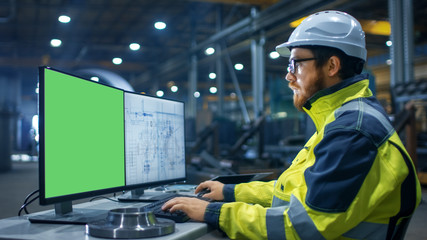 Inside the Heavy Industry Factory Industrial Engineer Works on the Personal Computer with Two Screen. One is Green Mock-up Screen and Other with Blueprints.