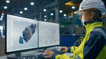 Wall Mural - Inside the Heavy Industry Factory Female Industrial Engineer Works on the Personal Computer on the Turbine/ Engine Project in 3D Using CAD Program.