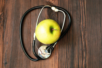 Medical stethoscope and apple on wooden background