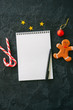 Festive Christmas background, white empty page of notepad, candy canes, gingerbread man, stars on a black stone background. Top view with copy space.