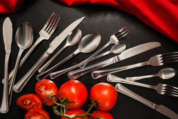 Silver cutlery set on black background with red color accents. Table setting for banquet concept