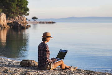 Wall Mural - Young woman using laptop computer on a beach. Freelance work concept