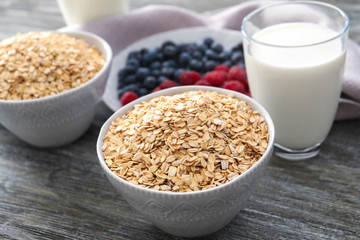 Bowls with oatmeal flakes and glass of milk on wooden background