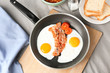 Frying pan with eggs, bacon and tomatoes on table