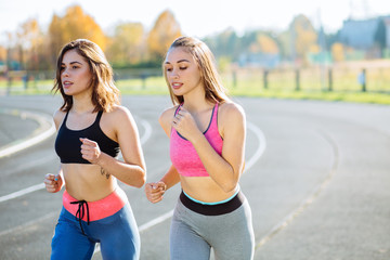 Two women exercising by jogging in the stadium track while sun is setting. Teenager healthy, sport and millennials people concept.