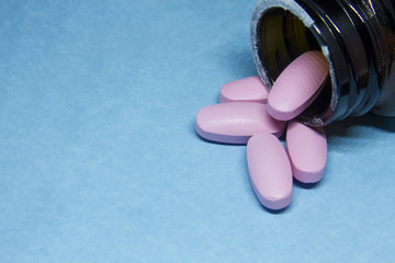 Pink pills in glass bottle on blue background