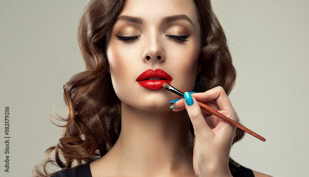  Makeup artist applies  red lipstick  . Beautiful woman face. Hand of make-up master, painting lips of young beautiful model. Makeup in progress
 - obrazy, fototapety, plakaty 