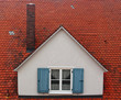 Białe okno z niebieskimi okiennicami na czerwonym dachu z kominem