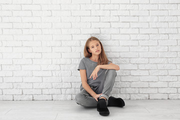 Wall Mural - Little fashionable girl sitting on floor near brick wall