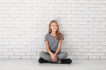 Wall Mural - Little fashionable girl sitting on floor near brick wall