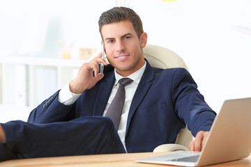 Canvas Print - Handsome businessman talking on mobile phone and using laptop while sitting in office