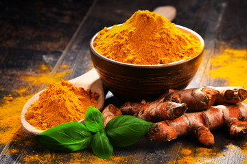 Composition with bowl of turmeric powder on wooden table