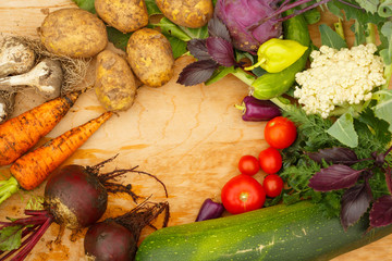 Wall Mural - Harvest of fresh vegetables on a wooden background, in garden background. Top view. Garlic, beet, zucchini, kohlrabi, cauliflower, pepper, tomatoes, potatoes, basil, cucumber, dill.