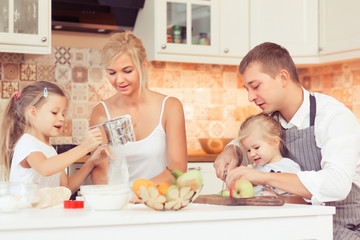 Young parents and their two beautiful and cute children girls cooking and eating breakfast ot lunch at kitchen table at home