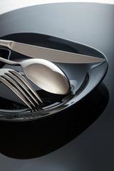 Wall Mural - Empty plate with knife and fork, spoon, on a black background