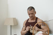 People, age, hobby and leisure concept. Portrait of concentrated elderly Caucasian man with grey hair and muscular arms with tattoo on shoulders focused on knitting, holding needles and brown wool