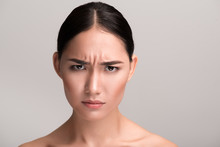 Full Of Anger. Close-up Portrait Of Young Naked Asian Girl Is Standing And Looking At Camera With Annoyance While Frowning Her Forehead. Isolated Background