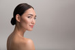 Fresh skin concept. Side view of elegant naked young asian woman is looking at camera with slight smile while demonstrating her perfect body. Isolated background with copy space in the right side