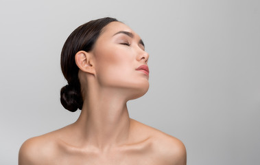 Being delight. Charming young asian girl is enjoying her clean and soft skin while posing naked with closed eyes. Isolated background with copy space in right side. Skincare concept