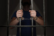 © vchalup - Arrested prisoner is holding bars in prison cell.