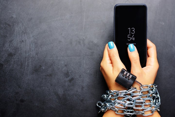woman hands tied with metallic chain with padlock on dark background suggesting internet or social m