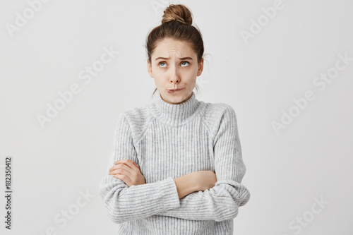 Valokuva Young lady with hair in topknot standing with arms folded looking up