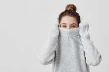 Portrait Of Girl Pulling Her Trendy Sweater Over Head Having Fun. Woman With Tied Hair In Topknot Being Childish Disappearing In Her Clothes Looking From Underneath. Happiness Concept