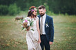 © shchus - The bride and groom stand leaning against each other. The bride with a wreath of fresh flowers and a bouquet against the backdrop of a summer forest glade.