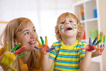 Wall Mural - Smiling child boy and his mother having fun and showing hands painted in colorful paints